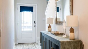 A hallway with a door, a mirror, two lamps, and a cabinet. - Coastal Retreat Just Steps From the Beach 🌴 (Port St. Joe)