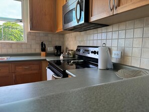 A kitchen with wooden cabinets, a stainless steel microwave, a gas stove, and a coffee maker. - Relaxing beachfront retreat, pool view balcony near Rainforest El Yunque (Río Grande)