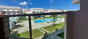 A view of a swimming pool with lounge chairs and a small palm tree, surrounded by a well-maintained lawn and a building with balconies. - Relaxing beachfront retreat, pool view balcony near Rainforest El Yunque (Río Grande)
