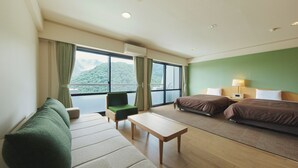 Ein Hotelzimmer mit einer Couch, zwei Betten, einem kleinen Tisch und Bergblick durch große Fenster.