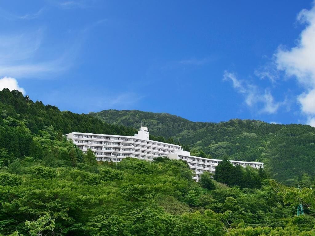 A large, multi-story building with a flat roof, surrounded by lush green hills.