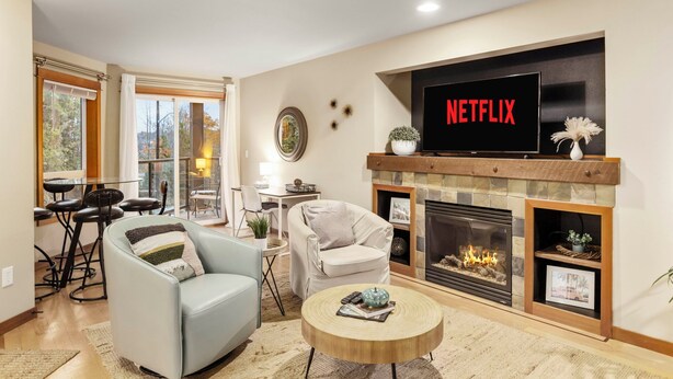 Een woonkamer met een open haard, een televisie erboven en een eethoek met een tafel en stoelen.