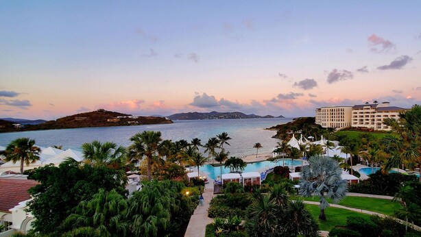 A resort with a pool, palm trees, and a view of the sea at sunset. - Oceanfront Ritz-Carlton Condo 2BR 2.5BA, Full Resort Amenities! (St Thomas)