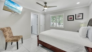 A bedroom with a bed, a chair, a ceiling fan, a TV, and a window with blinds. - New! Salty Steps - Naples Getaway with Hot Tub & Outdoor Kitchen (Naples)