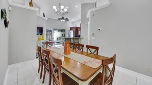 A dining area with a wooden table, chairs, and a chandelier. - New! Salty Steps - Naples Getaway with Hot Tub & Outdoor Kitchen (Naples)
