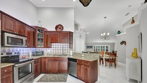 A spacious kitchen with wooden cabinets, stainless steel appliances, and a dining area with a chandelier. - New! Salty Steps - Naples Getaway with Hot Tub & Outdoor Kitchen (Naples)