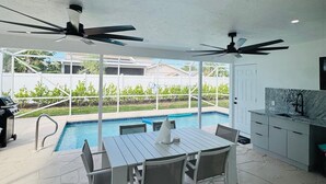 A modern kitchen with a marble countertop and a built-in sink, a dining area with a white table and chairs, and a pool area with a clear view of the surrounding greenery. - 3-bedroom house in fantastic Marco Island with AC (Marco Island)