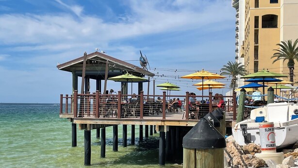 A pier with outdoor seating, a boat, and a building in the background. - NEW!! Rare 5 bedroom house w FREE HEATED POOL & HOT TUB 9 minutes to the beach!! (Seminole)