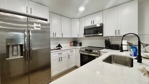 A modern kitchen with white cabinets, stainless steel appliances, and a marble countertop. - NEW!! Rare 5 bedroom house w FREE HEATED POOL & HOT TUB 9 minutes to the beach!! (Seminole)