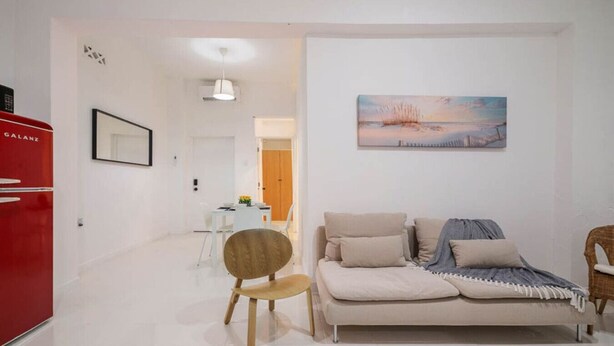 A modern living room with a sofa, a chair, a dining area, and a kitchen area with a red appliance. - Casa Luma No. 4 | Modern 2 Bedroom in San Juan PR (San Juan)