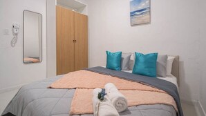 A bedroom with a bed, a wooden wardrobe, a mirror, and a painting of a beach. - Casa Luma No. 4 | Modern 2 Bedroom in San Juan PR (San Juan)