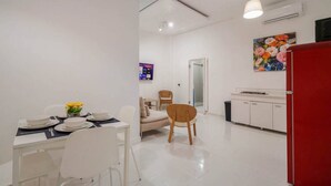 A modern kitchen with white cabinets, a red refrigerator, and a dining area with white chairs and a table set for two. - Casa Luma No. 4 | Modern 2 Bedroom in San Juan PR (San Juan)