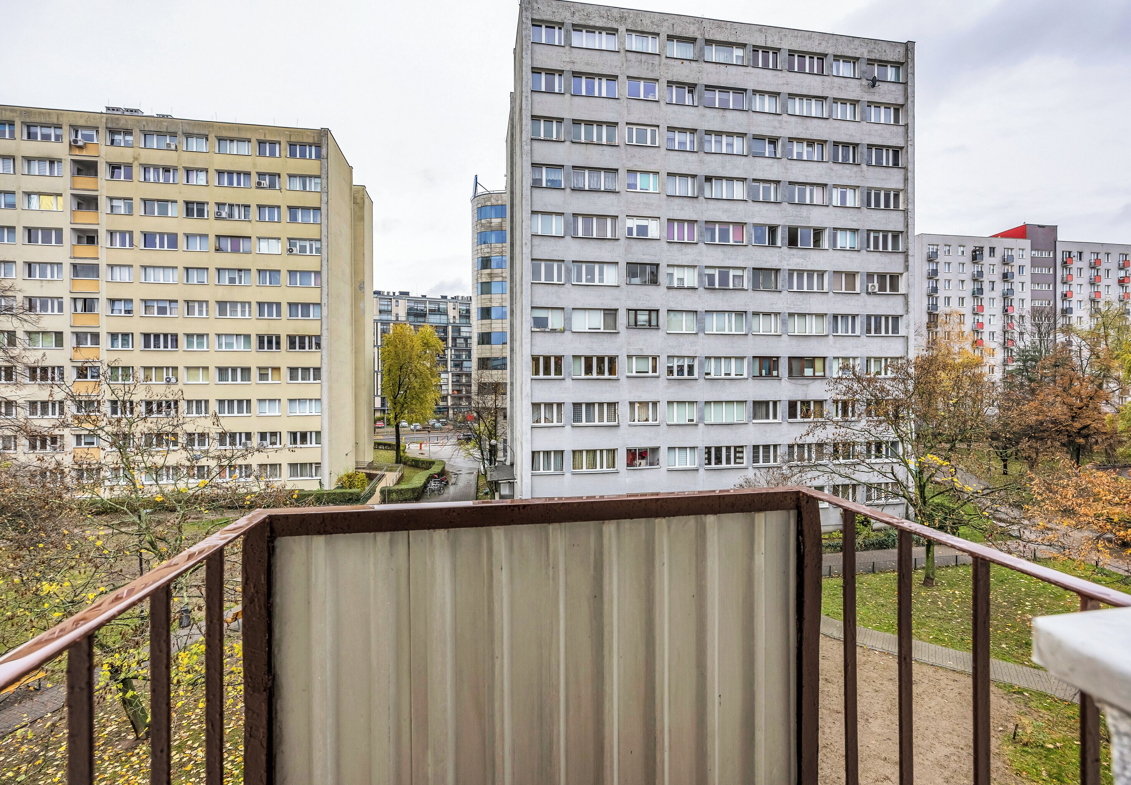 A high-rise residential building with multiple floors and balconies, surrounded by trees and a small park area.