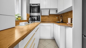 Een moderne keuken met witte kastjes, een houten aanrechtblad, een inbouwoven en een koffieapparaat.