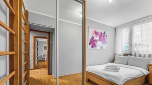 Een slaapkamer met een houten bed, een witte muur en een deur die naar een andere kamer leidt.