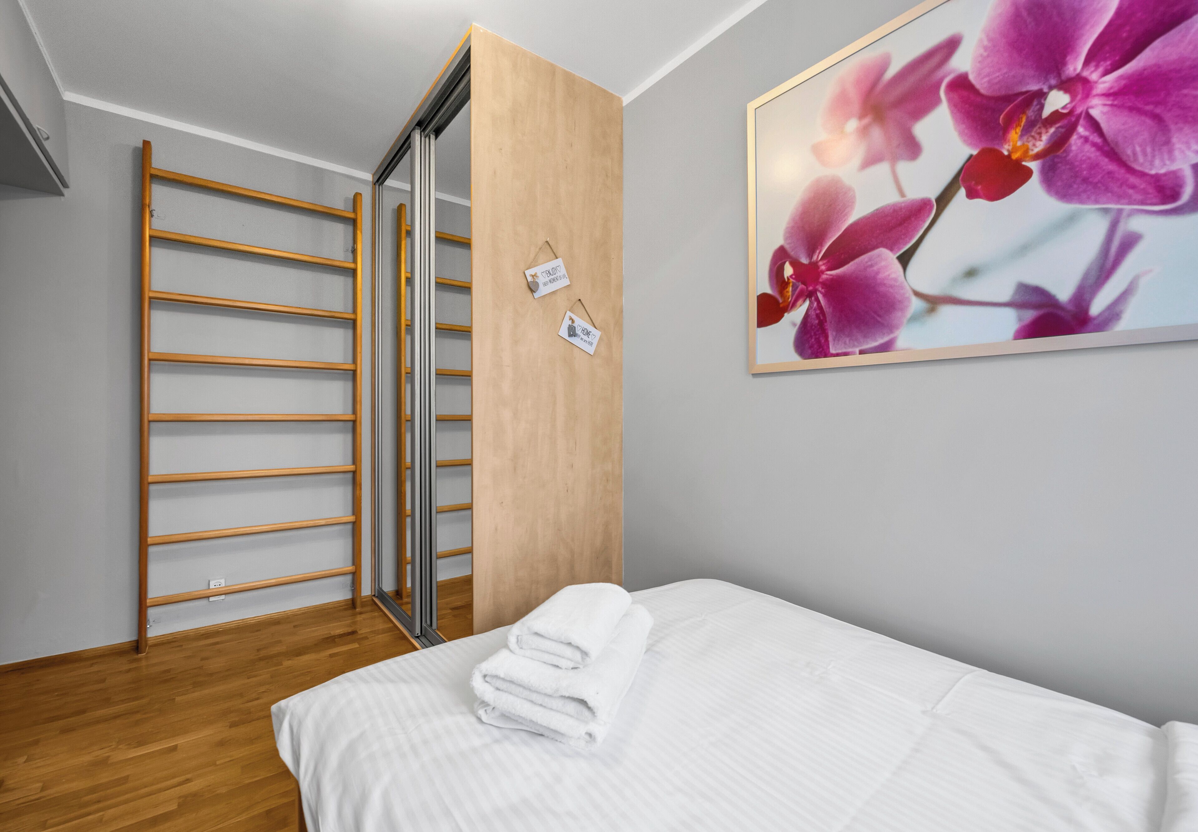 Une chambre à coucher avec un lit, une armoire en bois et un tableau représentant une orchidée, encadré.