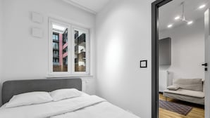 A modern bedroom with a bed, a window, a sofa, and a view of a building outside. - Kłobucka Deluxe Apartment (Warszawa)