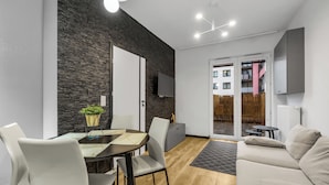 A modern living room with a dining area, a stone accent wall, a flat-screen TV, and a view of the outside. - Kłobucka Deluxe Apartment (Warszawa)