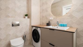 A modern bathroom with a washing machine, toilet, sink, and a mirror.