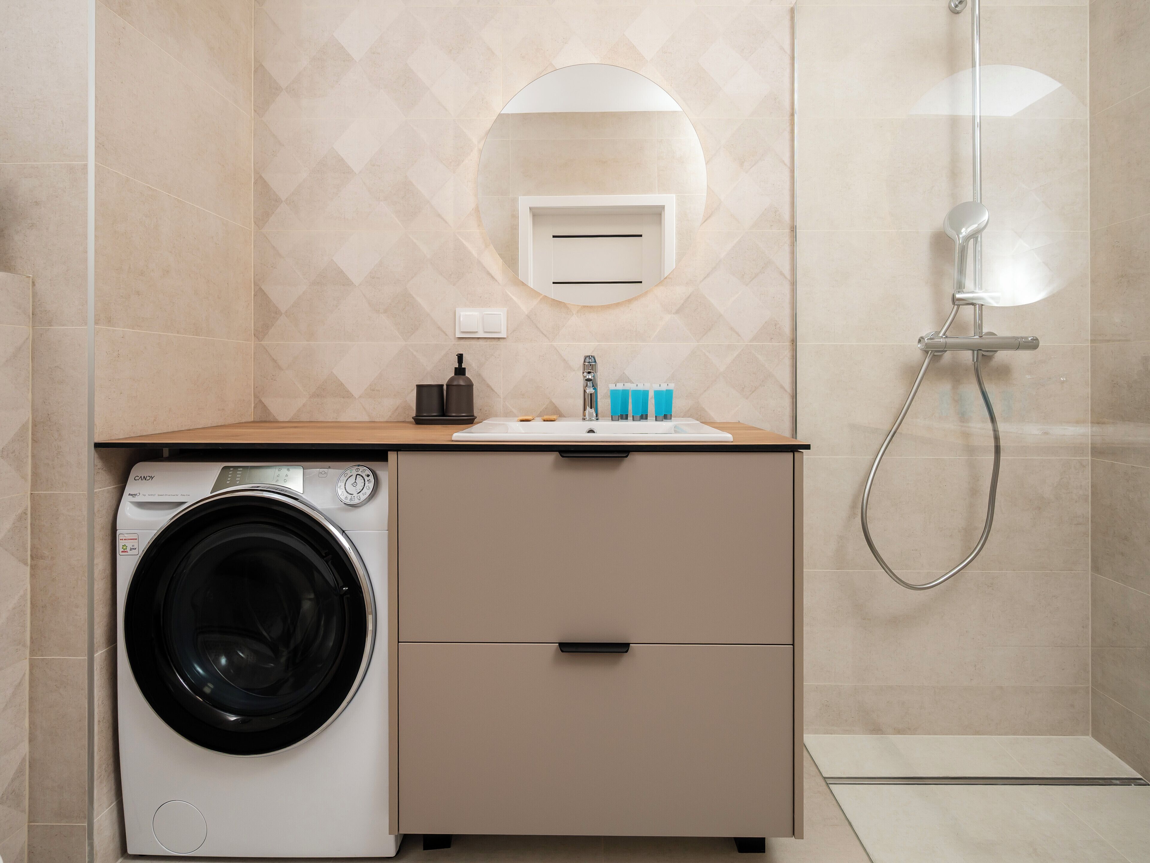 Een moderne badkamer met een wasmachine, een wastafel met toiletartikelen en een douche.