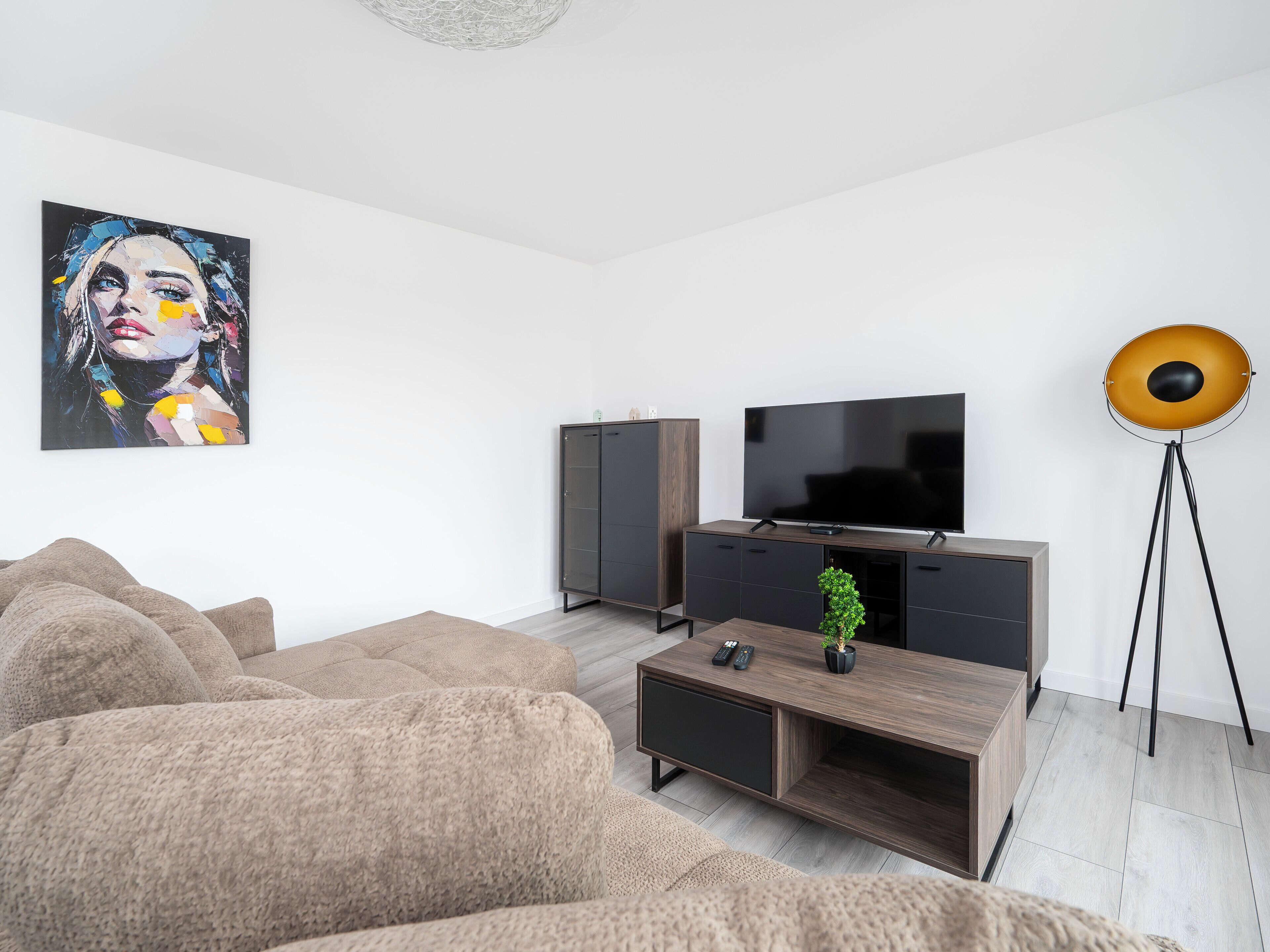 A modern living room with a large flat-screen TV, a dark wooden entertainment unit, a beige sofa, and a floor lamp.