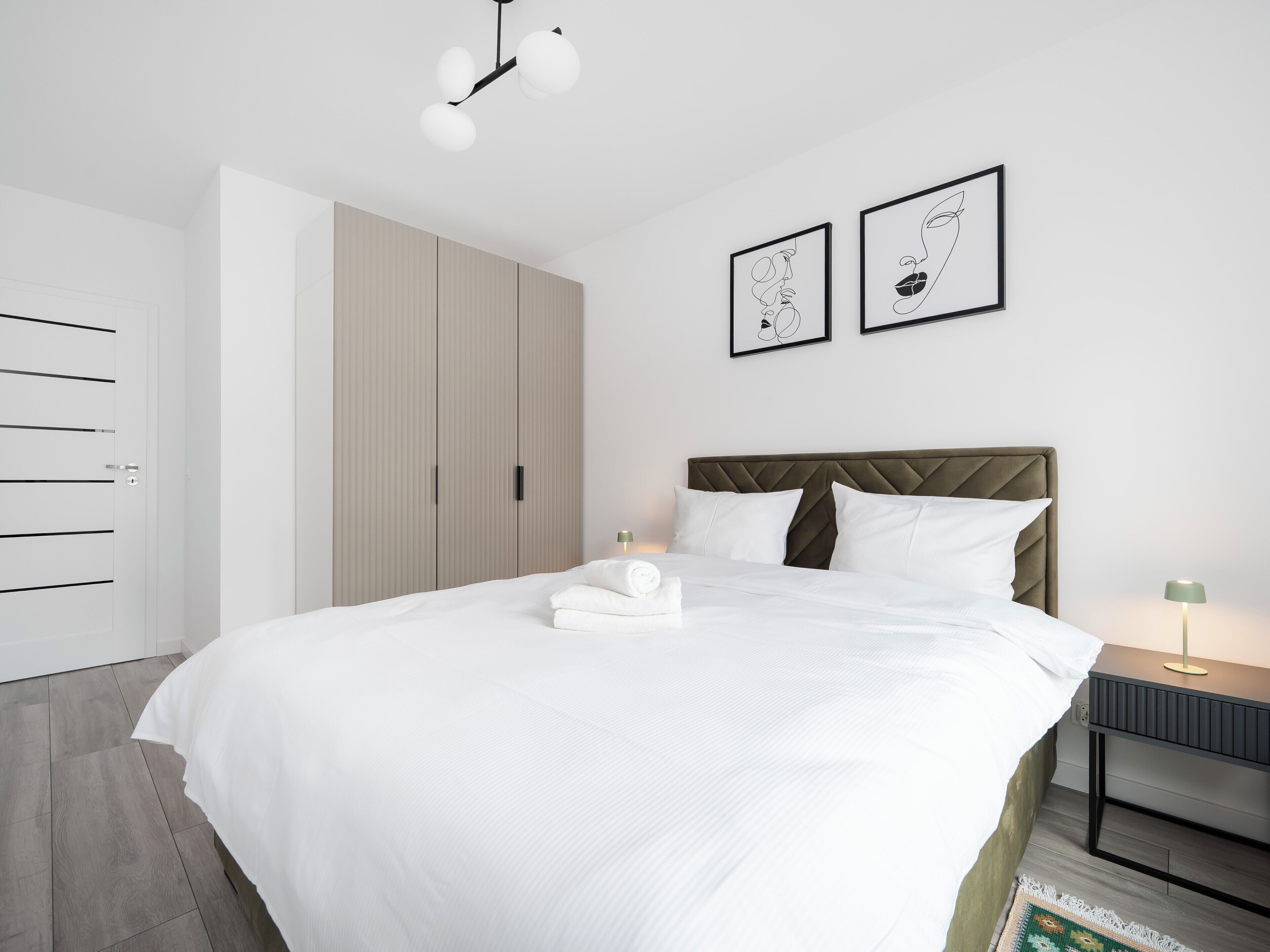 A modern bedroom with a large bed, a wardrobe, and two framed artworks on the wall.