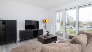 Un salon moderne doté d’un grand téléviseur à écran plat, de meubles en bois foncé et d’une grande fenêtre donnant sur un paysage urbain.