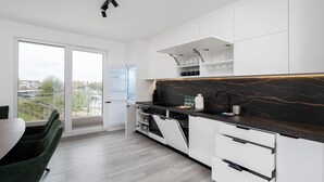 Une cuisine moderne avec des meubles blancs, un pare-feu en marbre noir et une vue sur la ville grâce à de grandes fenêtres.
