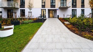 Un immeuble d’appartements moderne doté d’une entrée principale, d’un espace extérieur aménagé pour s’asseoir et d’un jardin bien entretenu.