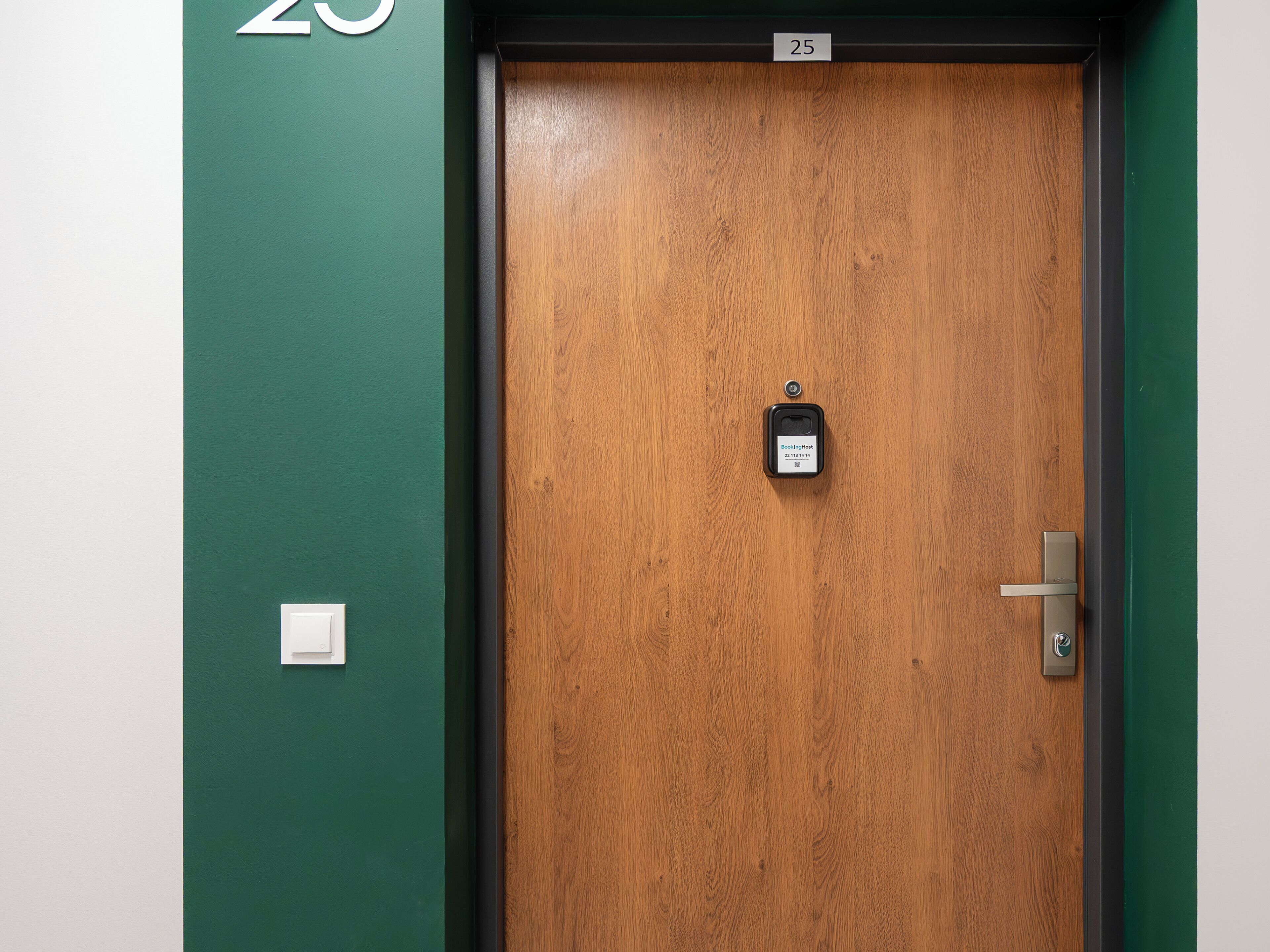 A wooden door with a lock and a keyhole, a door number sign, and a light switch on the wall.