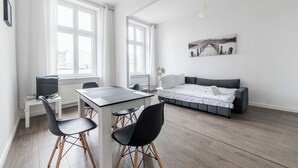 Ein modernes, helles Zimmer mit Esstisch, Stühlen, einer Couch und einem Bett.