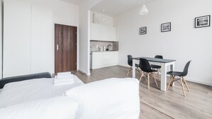 Ein modernes Hotelzimmer mit Bett, einer kleinen Küchenzeile, einem Essbereich mit Tisch und Stühlen sowie Holzboden.