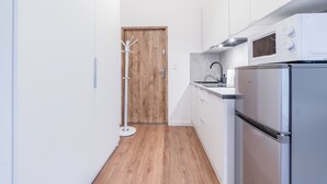A narrow kitchen with white cabinets, a wooden door, a stainless steel refrigerator, and a microwave. - Heart of Poznań Studio #3 (Poznań)