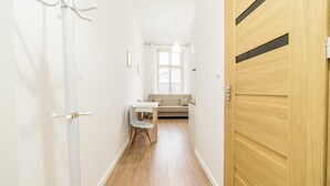 Ein Flur mit einer Holztür, einem weißen Kleiderständer, einem weißen Tisch mit einem Stuhl und einer Couch im Hintergrund.