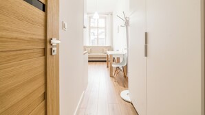 En hall med en dörr av trä, en vit vägg, ett vitt golv, ett vitt bord med en stol och ett fönster med gardiner.