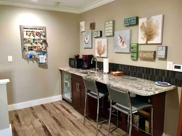 A modern kitchen with a granite countertop, bar stools, and various wall art. - Downtown Guilford Studio - Walk to Green, Beach & Train (Guilford)