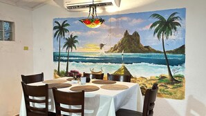Un coin repas avec une table dressée pour quatre personnes, une fresque représentant une scène de plage et un luminaire suspendu.