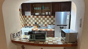 Une cuisine compacte équipée d’une cuisinière intégrée, d’un four à micro-ondes et d’un réfrigérateur. Il y a quatre tabourets au comptoir et une pancarte sur laquelle on peut lire « À MANGER ».