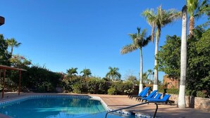 Une piscine bordée de chaises longues bleues et de palmiers.