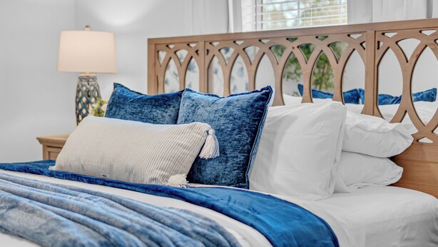 Een bed met blauw-witte beddengoed, een houten hoofdbord en een nachtkastje met een lamp.