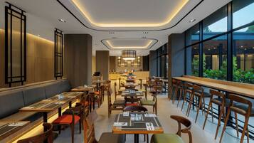 A modern restaurant with a long counter, multiple tables, and chairs. There are large windows on one side and a kitchen area in the center.