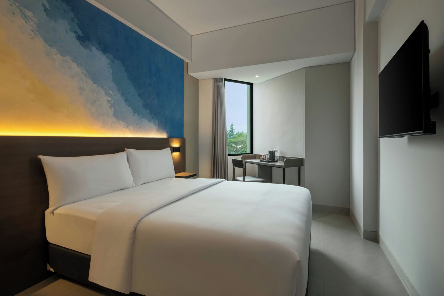Een hotelkamer met een groot bed, een bureau, een stoel, een televisie en een raam met uitzicht op groen.