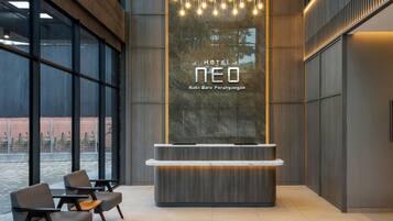 A modern hotel reception area with a large glass window, a reception desk, and a seating area with chairs.