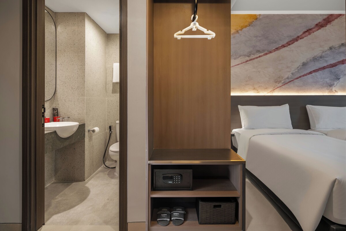Une chambre d’hôtel comprenant une salle de bain, un lit, une étagère avec un panneau de commande et une œuvre d’art murale.