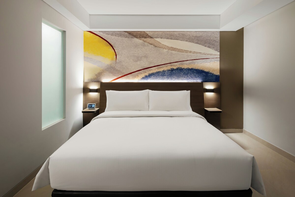 Une chambre d’hôtel moderne avec un grand lit, une table de chevet et une fresque murale.