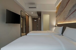 Habitación de hotel con dos camas, un televisor de pantalla plana montado en la pared y un diseño moderno con una gran obra de arte en la pared.