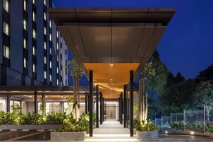 Una entrada de hotel moderna con un corredor cubierto, ventanas amplias y un sendero bien iluminado que conduce al edificio.