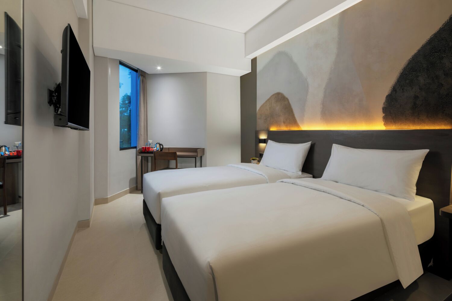 A modern hotel room with two beds, a desk, and a TV.