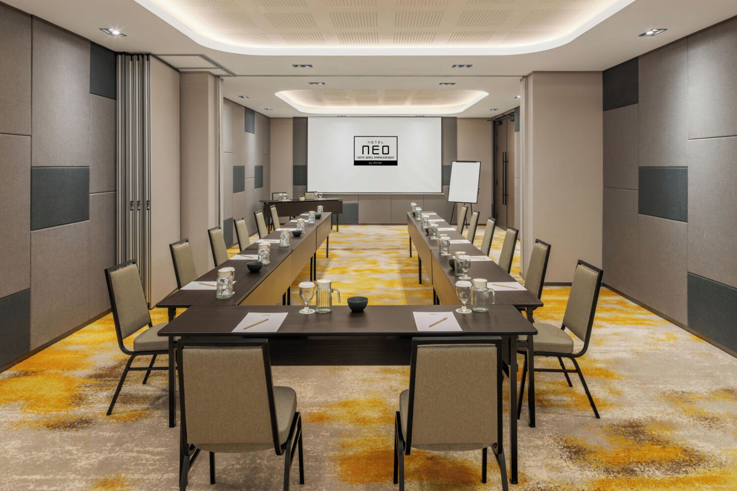 A conference room with a long table, chairs, a projector screen, and a carpeted floor.