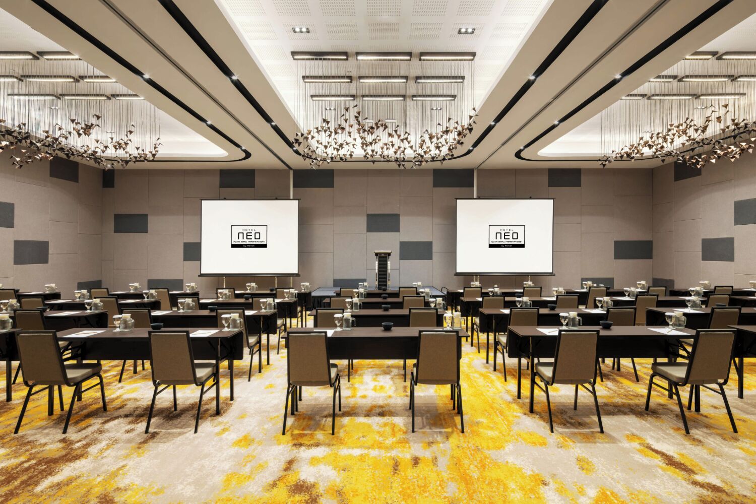 Une salle de conférence équipée de plusieurs tables et chaises, de deux grands écrans et d’un lustre.